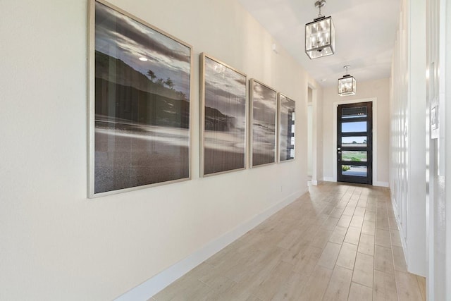 hallway featuring a chandelier, wood finished floors, and baseboards