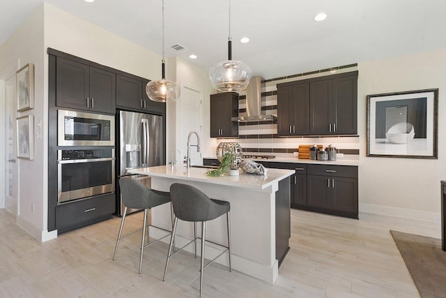 kitchen featuring ventilation hood, appliances with stainless steel finishes, light countertops, a sink, and a breakfast bar area