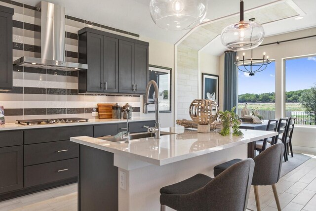 kitchen featuring tasteful backsplash, a chandelier, exhaust hood, stainless steel gas cooktop, and pendant lighting
