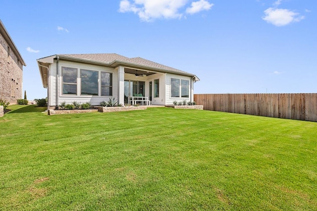 rear view of property featuring fence, a lawn, and a ceiling fan