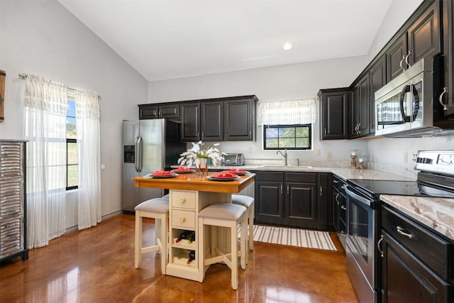 kitchen featuring light stone counters, finished concrete flooring, lofted ceiling, stainless steel appliances, and a sink