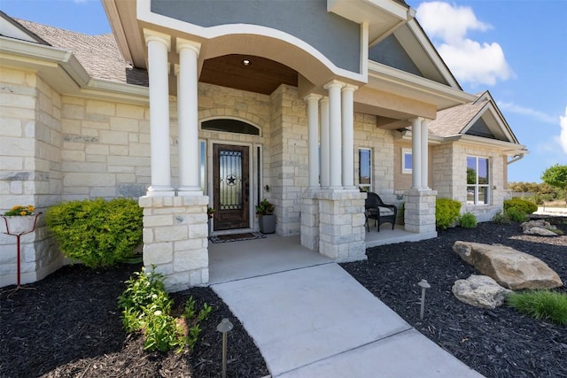 property entrance featuring a porch, roof with shingles, and stone siding
