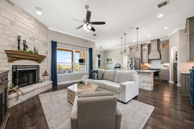 living room featuring crown molding, a fireplace, dark wood finished floors, a ceiling fan, and visible vents