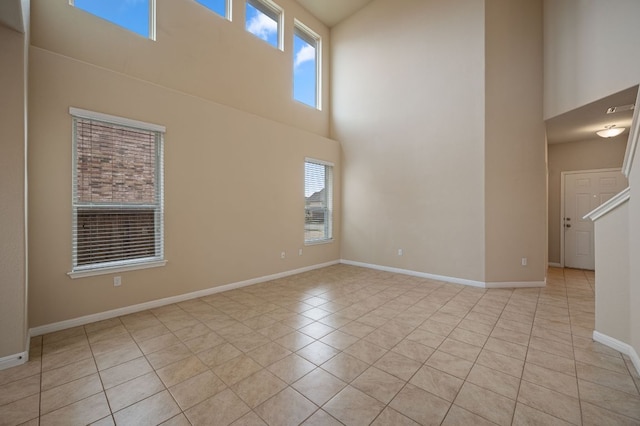 unfurnished room featuring a healthy amount of sunlight, light tile patterned flooring, a towering ceiling, and baseboards