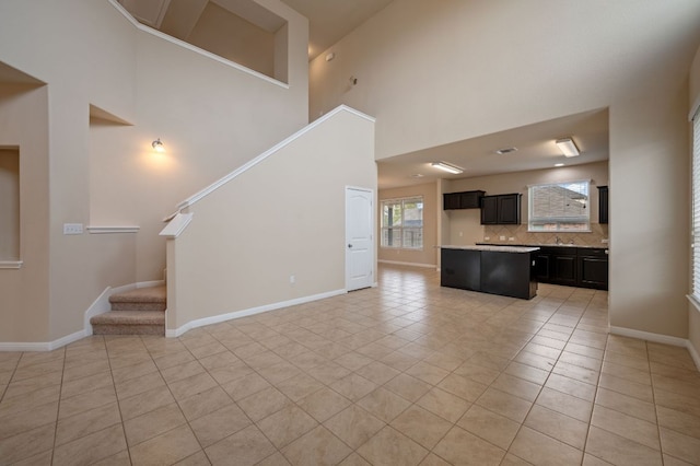 unfurnished living room with light tile patterned floors, baseboards, a towering ceiling, and stairs