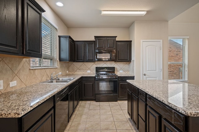 kitchen with light tile patterned floors, backsplash, black appliances, light stone countertops, and a sink