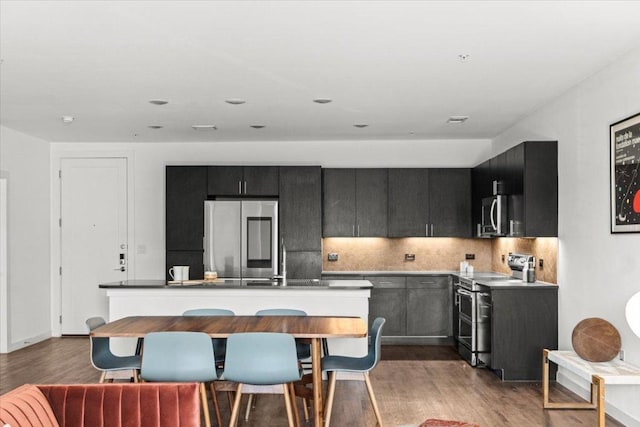 kitchen featuring stainless steel appliances, light wood finished floors, dark cabinets, and decorative backsplash