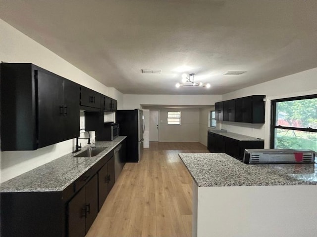 606 Springdale Rd, Austin, TX 78702 - kitchen with a sink, dark cabinetry, stainless steel appliances, light wood finished floors, and light stone countertops