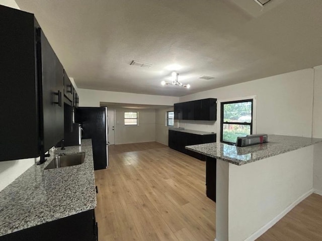 606 Springdale Rd, Austin, TX 78702 - kitchen with dark cabinets, a sink, freestanding refrigerator, light wood finished floors, and light stone countertops