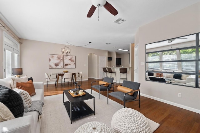 living area with visible vents, arched walkways, wood finished floors, and ceiling fan with notable chandelier
