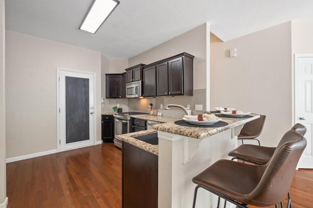 kitchen with dark wood-style flooring, light stone counters, a breakfast bar area, decorative backsplash, and appliances with stainless steel finishes