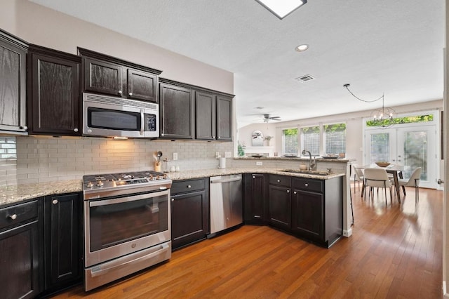 kitchen featuring tasteful backsplash, a sink, light wood-style floors, a peninsula, and stainless steel appliances
