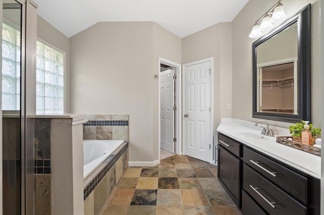 full bathroom featuring a garden tub, vanity, baseboards, and stone finish flooring
