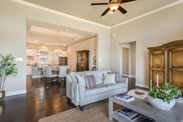 living room featuring visible vents, a tray ceiling, baseboards, dark wood-style flooring, and ceiling fan with notable chandelier