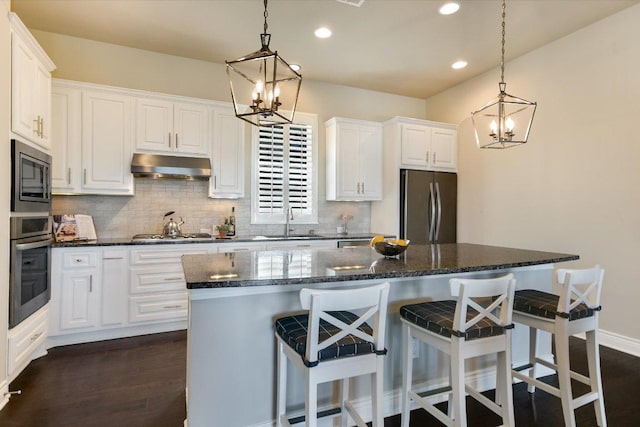 kitchen featuring an inviting chandelier, stainless steel appliances, under cabinet range hood, backsplash, and a sink