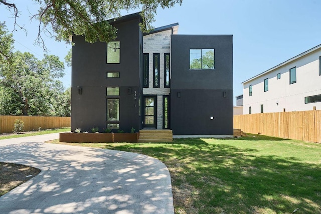modern home featuring stucco siding, fence, and a front yard