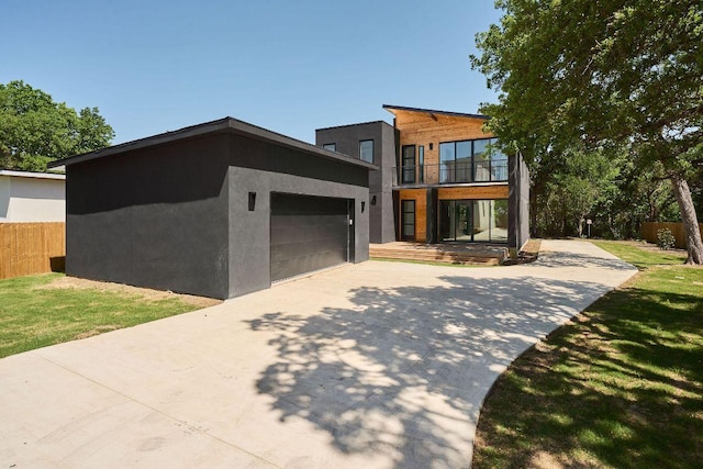 contemporary house with stucco siding, fence, a balcony, an attached garage, and driveway
