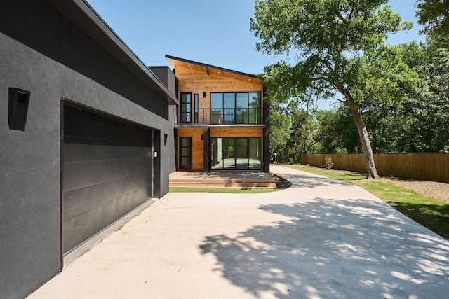 view of side of property with a balcony, fence, a patio, stucco siding, and driveway