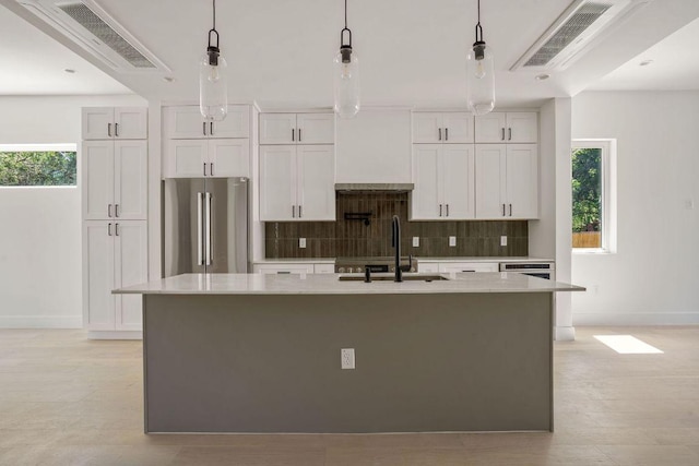 kitchen featuring baseboards, a sink, freestanding refrigerator, a kitchen island with sink, and backsplash