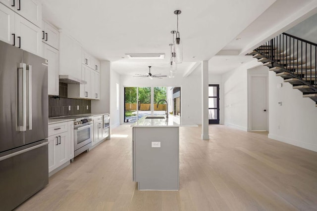 kitchen with tasteful backsplash, light wood-type flooring, high quality appliances, open floor plan, and a sink