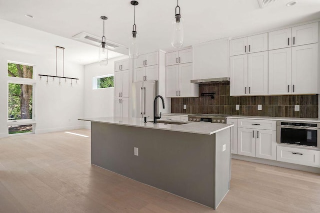 kitchen featuring light wood-style flooring, a sink, appliances with stainless steel finishes, custom range hood, and decorative backsplash