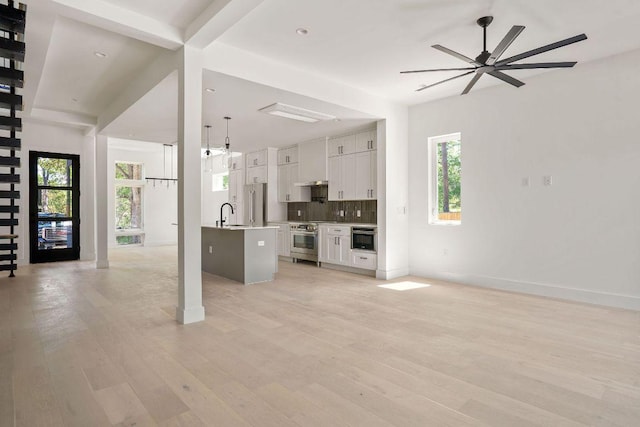 unfurnished living room featuring a sink, light wood finished floors, baseboards, and a ceiling fan