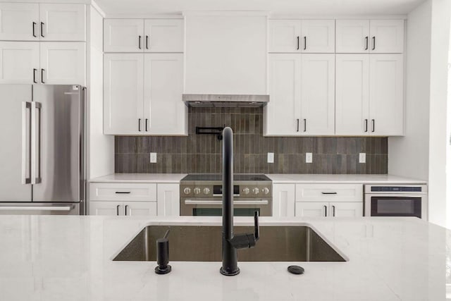 kitchen with backsplash, white cabinets, light stone counters, and premium appliances