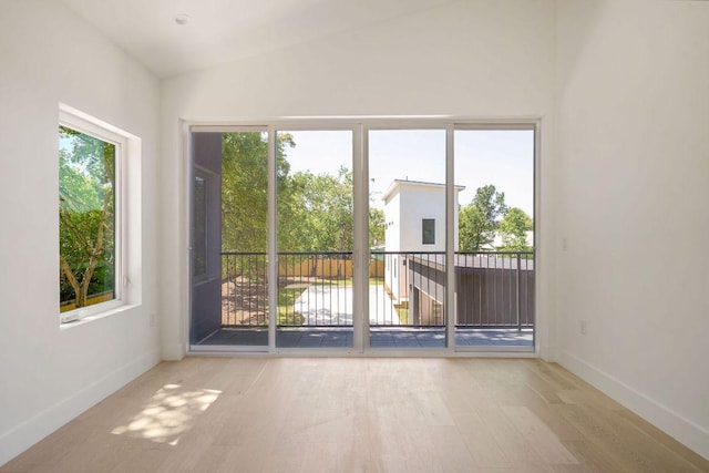spare room featuring a wealth of natural light, vaulted ceiling, wood finished floors, and baseboards