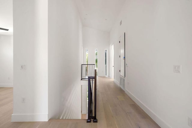 corridor featuring light wood-style flooring, baseboards, and an upstairs landing