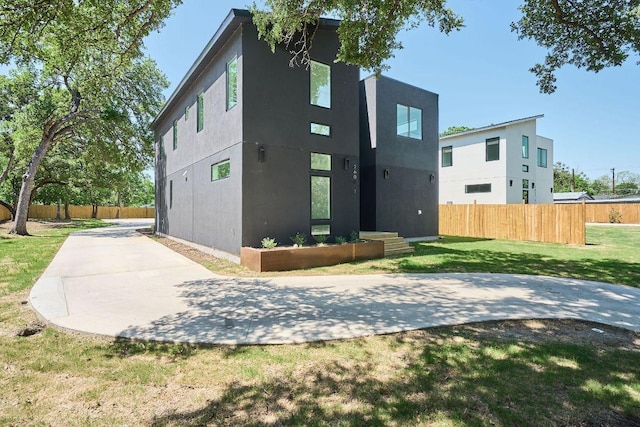 rear view of property featuring a patio area, stucco siding, fence, and a lawn