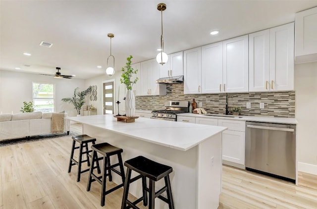 6007 Belfast Dr, Austin, TX 78723 - kitchen featuring stainless steel appliances, under cabinet range hood, light wood finished floors, white cabinetry, and decorative backsplash