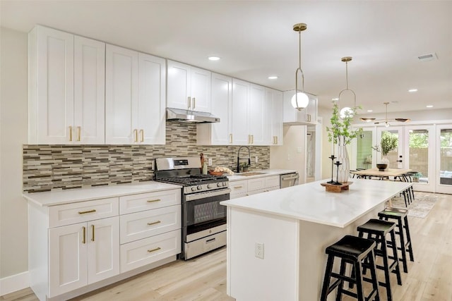 6007 Belfast Dr, Austin, TX 78723 - kitchen featuring stainless steel appliances, under cabinet range hood, a kitchen island, light wood-style floors, and recessed lighting