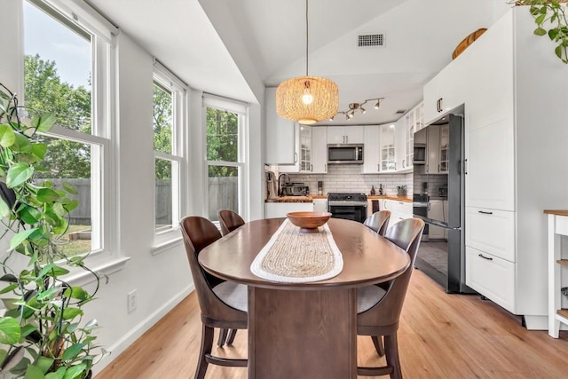 dining room featuring light wood finished floors, baseboards, vaulted ceiling, and rail lighting