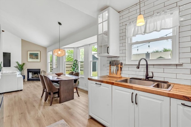 kitchen with a sink, wood counters, vaulted ceiling, white cabinets, and tasteful backsplash