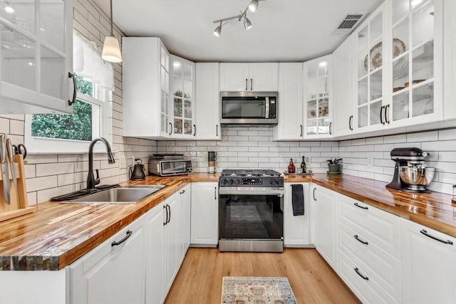 206 Quail Cir, Hutto, TX 78634 - kitchen with butcher block counters, stainless steel appliances, white cabinets, hanging light fixtures, and tasteful backsplash
