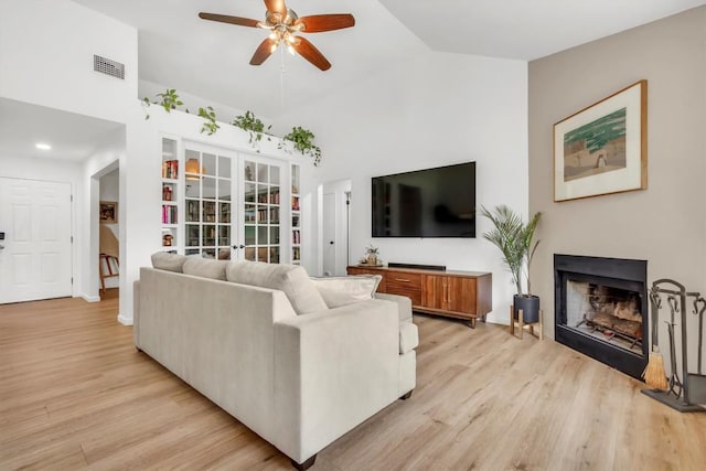 living area featuring french doors, ceiling fan, light wood-type flooring, a fireplace, and high vaulted ceiling