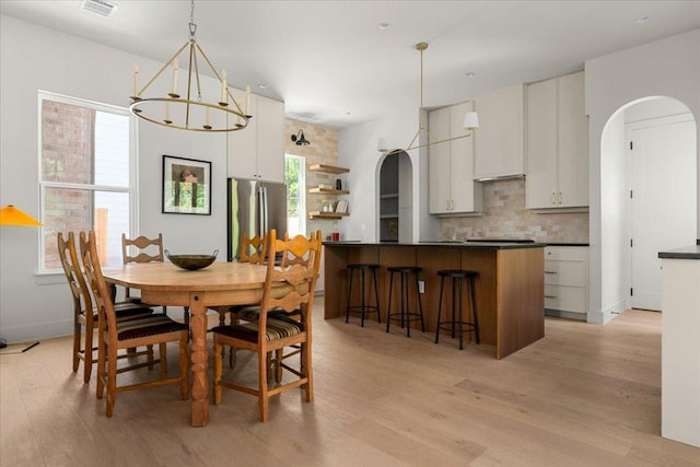 dining room with arched walkways, light wood-type flooring, a chandelier, and healthy amount of natural light