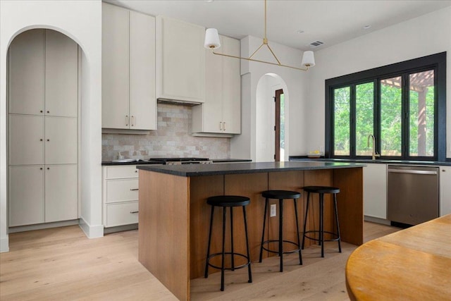 kitchen featuring arched walkways, stainless steel dishwasher, light wood-style floors, and a kitchen island