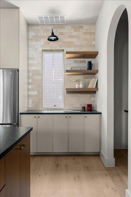 kitchen featuring freestanding refrigerator, light wood-style flooring, dark countertops, arched walkways, and baseboards