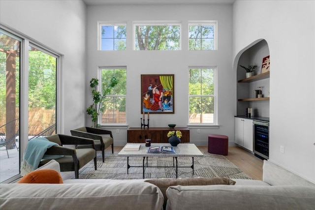 living room with beverage cooler, plenty of natural light, light wood-type flooring, and a towering ceiling