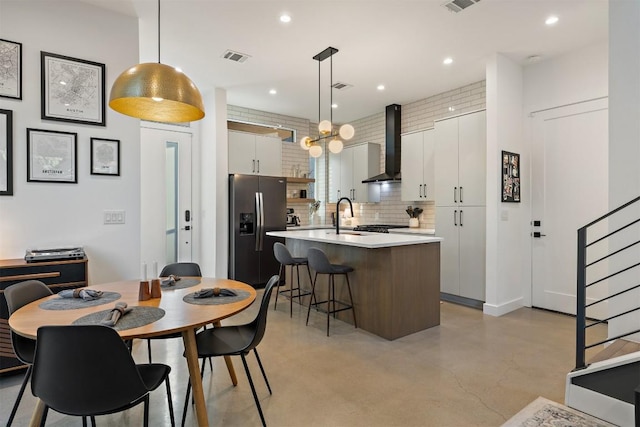4907 Delores Ave, Austin, TX 78721 - kitchen with stainless steel fridge, wall chimney exhaust hood, light countertops, finished concrete flooring, and an island with sink