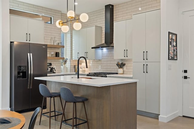 4907 Delores Ave, Austin, TX 78721 - kitchen with stainless steel fridge, wall chimney range hood, decorative backsplash, light countertops, and an island with sink