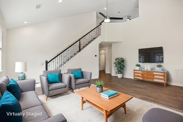 living area with a high ceiling, wood finished floors, a ceiling fan, baseboards, and stairs