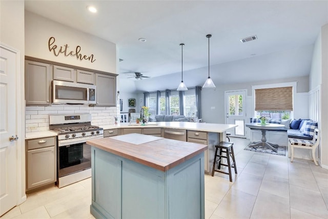 kitchen with open floor plan, wood counters, appliances with stainless steel finishes, and a peninsula
