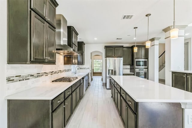 18705 Alonso Pl, Austin, TX 78738 - kitchen featuring stainless steel appliances, wall chimney range hood, a large island, decorative backsplash, and arched walkways