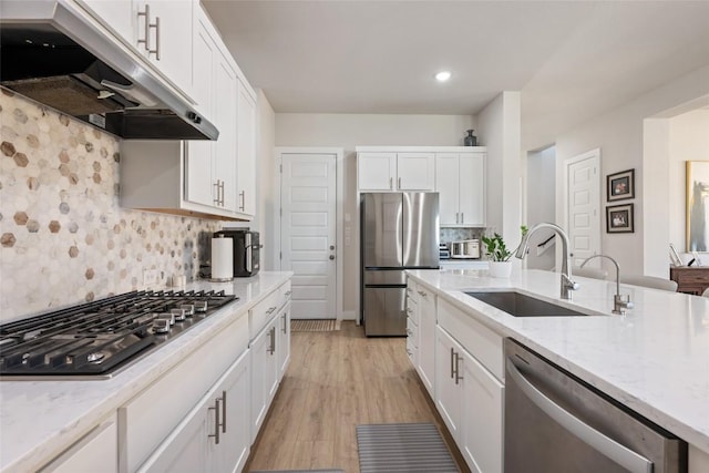 kitchen featuring stainless steel appliances, a sink, under cabinet range hood, white cabinetry, and tasteful backsplash