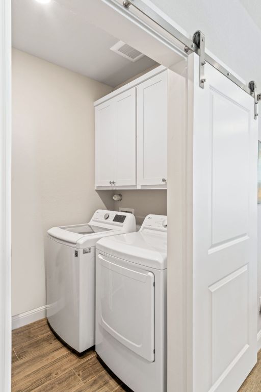 laundry area with baseboards, washing machine and dryer, a barn door, cabinet space, and light wood finished floors