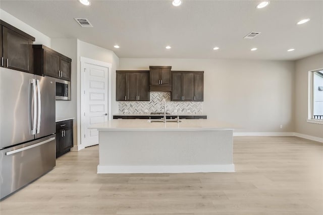 508 Saturnia Cv, Georgetown, TX 78628 - kitchen featuring stainless steel appliances, an island with sink, backsplash, light wood-style flooring, and light countertops