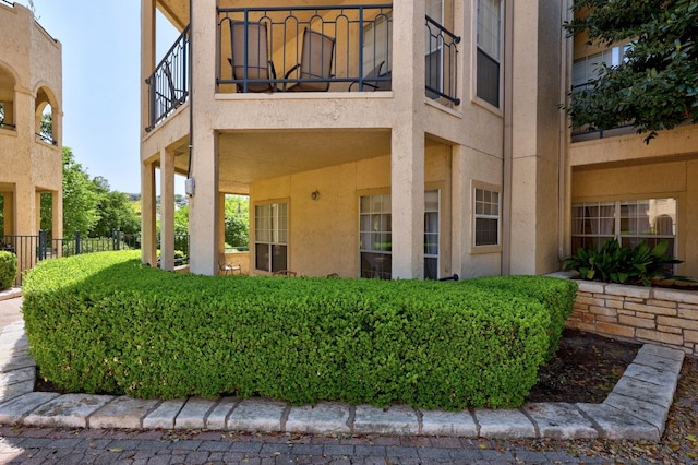 view of exterior entry with a balcony, fence, and stucco siding
