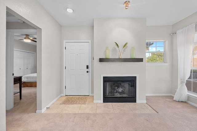 carpeted foyer featuring baseboards, a ceiling fan, tile patterned flooring, and a glass covered fireplace